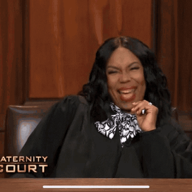 a woman in a judge 's robe is sitting at a table in a court room .