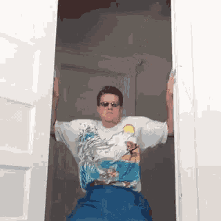 a man wearing sunglasses and a simpson shirt is standing in an open doorway .
