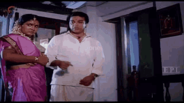 a man and a woman are standing next to each other in a room . the woman is wearing a pink sari .