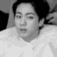 a black and white photo of a man laying on a bed with a towel around his neck .