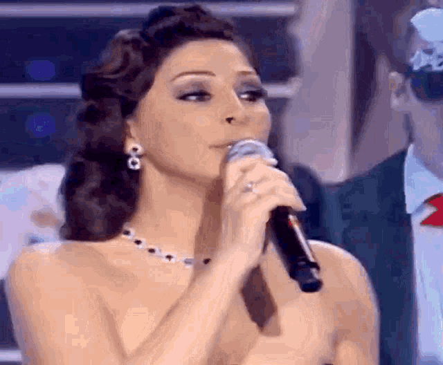a woman is singing into a microphone while wearing earrings and a necklace .
