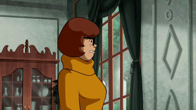 a woman in a yellow sweater stands in front of a window in a room