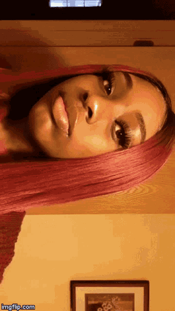 a woman with pink hair is standing in front of a wall with a picture of a flower on it