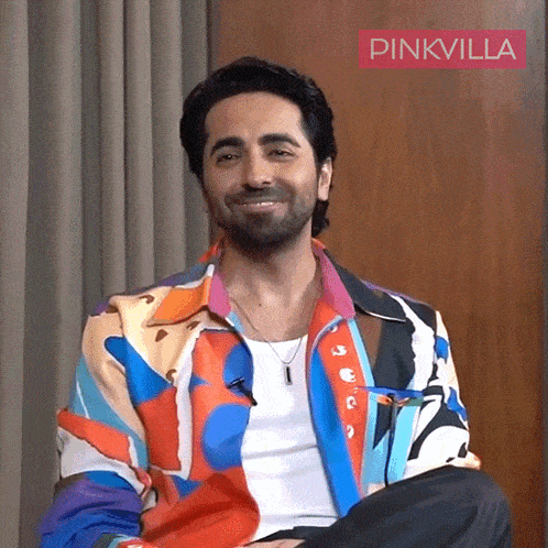 a man wearing a colorful jacket is smiling in front of a pinkvilla logo