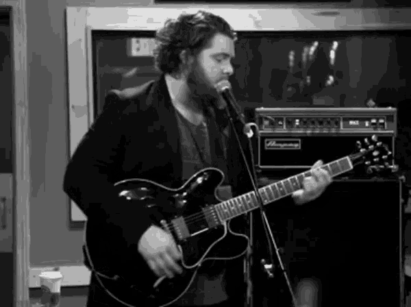 a man singing into a microphone while playing a guitar in front of an amp that says ampeg