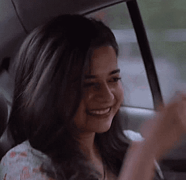 a woman is sitting in the back seat of a car waving her hand .