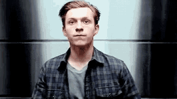 a man in a plaid shirt is standing in front of a wall and looking at the camera .
