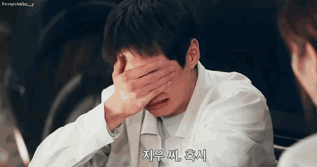 a man in a white shirt is covering his face with his hand .