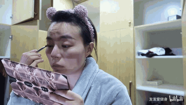 a woman wearing a headband is applying makeup and holding a palette that says ' naked ' on it