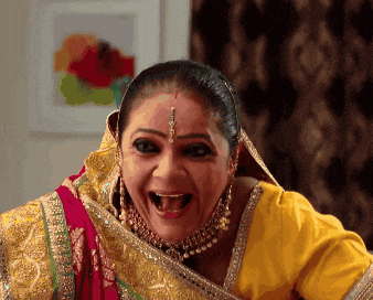 a woman wearing a yellow top and a red and gold sari is making a funny face