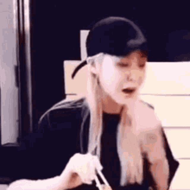 a woman wearing a baseball cap and eating noodles with chopsticks .