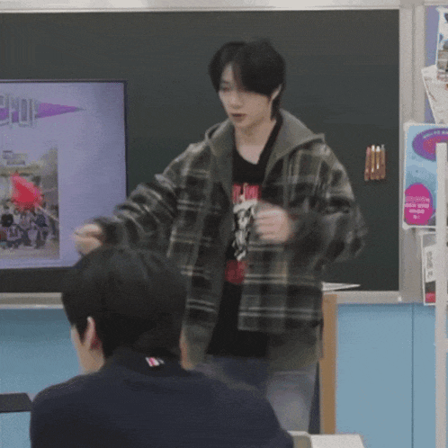 a man in a plaid jacket is standing in front of a blackboard with a picture of a rocket on it