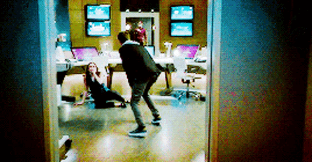a man and a woman are standing in a room with a lot of monitors on the wall