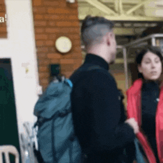 a man with a backpack and a woman in a red jacket are standing next to each other .