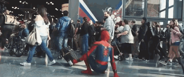 a man in a spiderman costume is kneeling down in a crowd of people