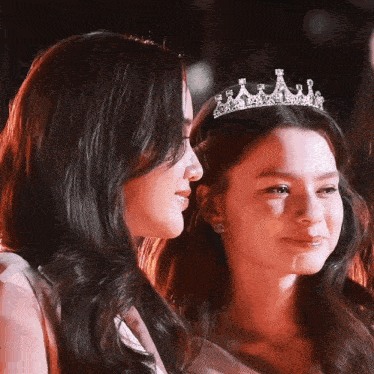 a woman wearing a tiara stands next to another woman wearing a tiara