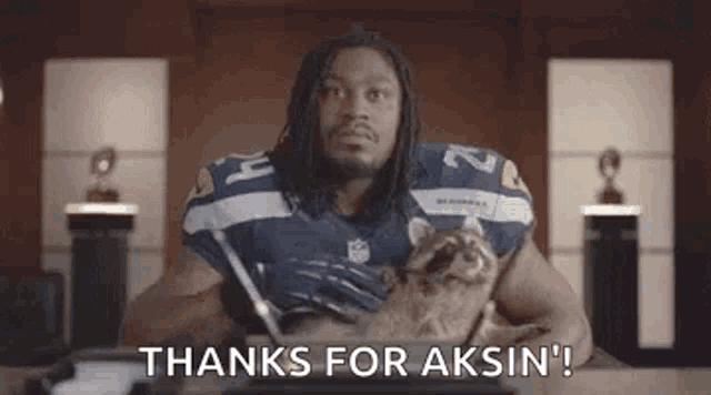 a football player is sitting at a desk holding a cat and saying `` thanks for akin '' .
