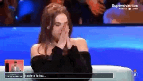 a woman is crying while sitting on a couch in front of a television screen .