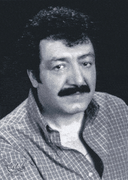 a man with curly hair and a mustache is wearing a plaid shirt and has the word nisantes on the bottom left