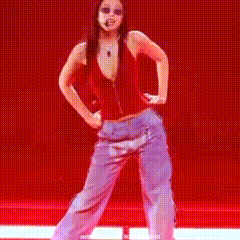 a woman in a red tank top and purple pants is dancing on a stage .