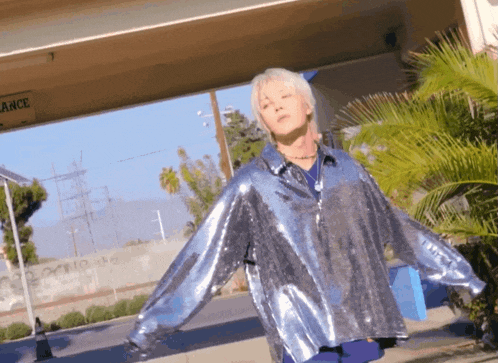 a person wearing a silver sequined shirt is standing in front of a sign that says ' arce ' on it
