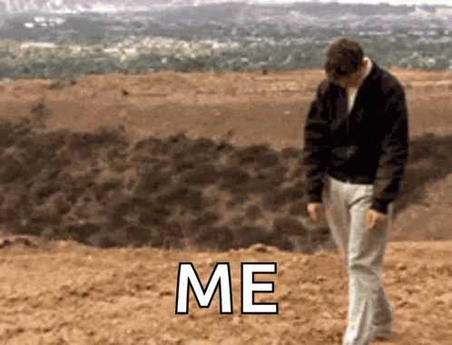 a man in a black jacket is walking in the dirt with the word me written on the ground behind him