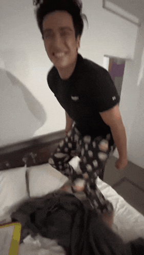 a man in a black shirt is standing on a bed .