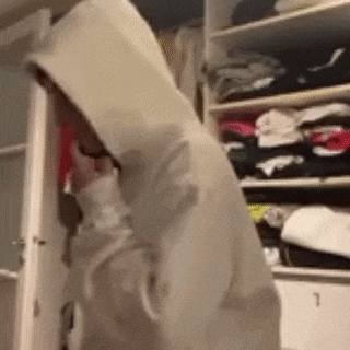 a person wearing a hoodie is standing in a closet .