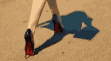 a woman wearing red high heels is walking on a sandy surface .