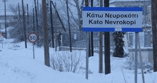 a blue sign is sitting in the snow in front of a snow covered forest .