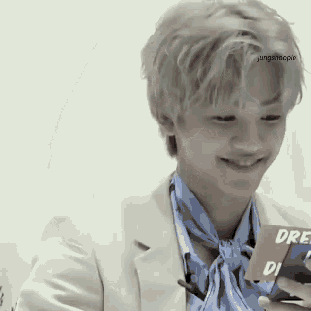 a young man wearing a white jacket and a blue scarf is smiling while holding a card .