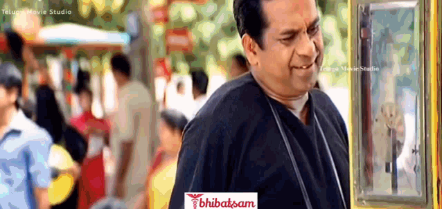 a man in a black shirt is smiling in front of a telugu movie studio sign