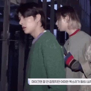 a man and a woman are standing next to each other in a room . the man is wearing a green sweater .