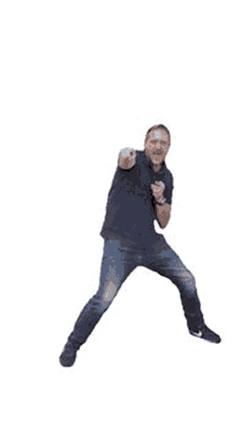 a man in a black shirt and blue jeans is jumping in the air while dancing .
