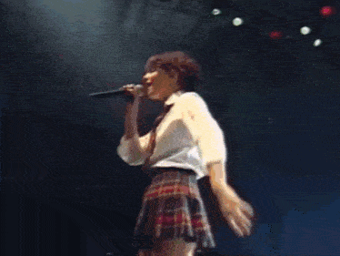 a woman in a plaid skirt is singing into a microphone on a stage