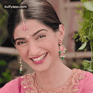 a woman wearing a pink dress and earrings is smiling .
