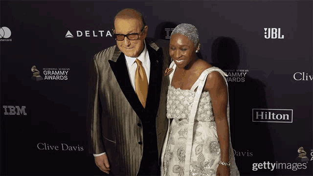 a man and woman pose on a red carpet in front of a delta and hilton advertisement