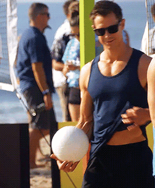 a man in a blue tank top holds a volleyball