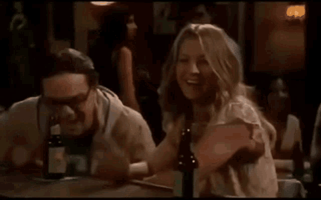a man and a woman are sitting at a table laughing and drinking beer .