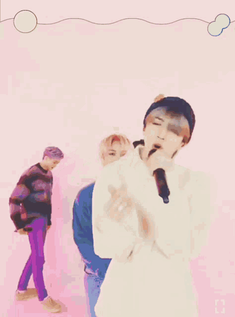 a man is singing into a microphone in front of a pink background