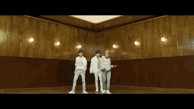 three men are standing in a room with wooden walls and a ceiling .