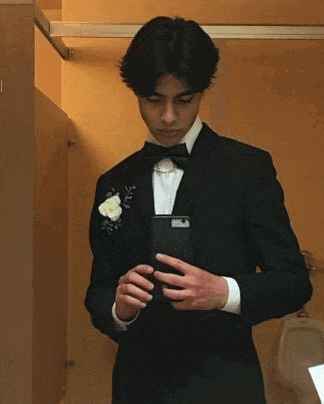 a young man in a tuxedo and bow tie is taking a selfie in a bathroom .