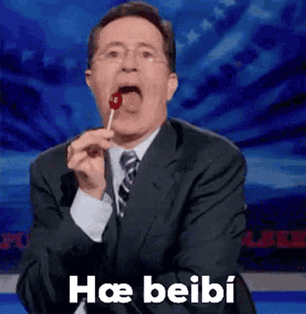 a man in a suit and tie is eating a lollipop and says hae beibi .
