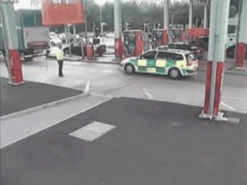 a man in a yellow vest is standing in a parking lot next to a gas pump .