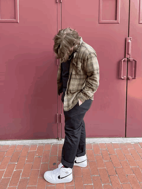 a man wearing a plaid shirt and black pants is standing in front of a red door