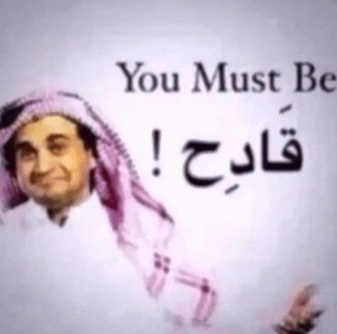 a man wearing a pink scarf is standing in front of a sign that says " you must be " .