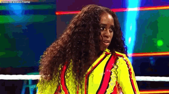a woman with long curly hair is standing in a boxing ring wearing a yellow and red outfit .