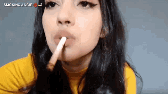 a woman is smoking a cigarette in a yellow shirt .