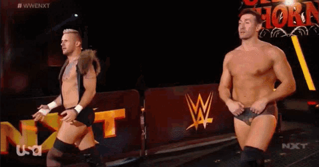 two men are walking in front of a sign that says nxt