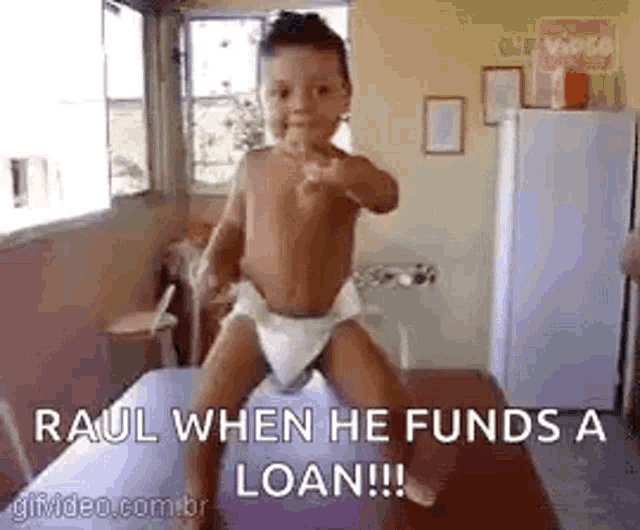 a baby in a diaper is pointing at the camera while sitting on a bed .